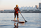 A person peacefully paddling on a board in the water with Vancouver Water Adventures in the background.